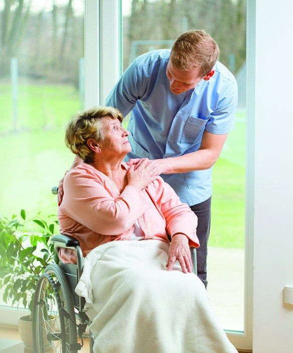 A male nurse comforts an elderly woman seated in a wheelchair