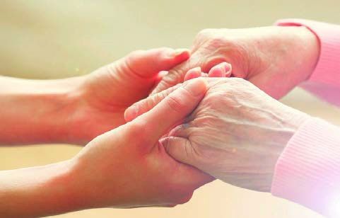 A caregiver gently holds the hands of an older person